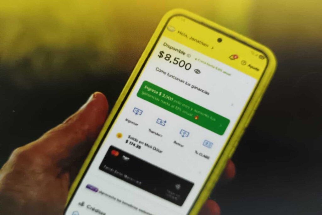 Hand holding a yellow phone displaying a finance app with a prominent $8,500 balance and green action banner at center.