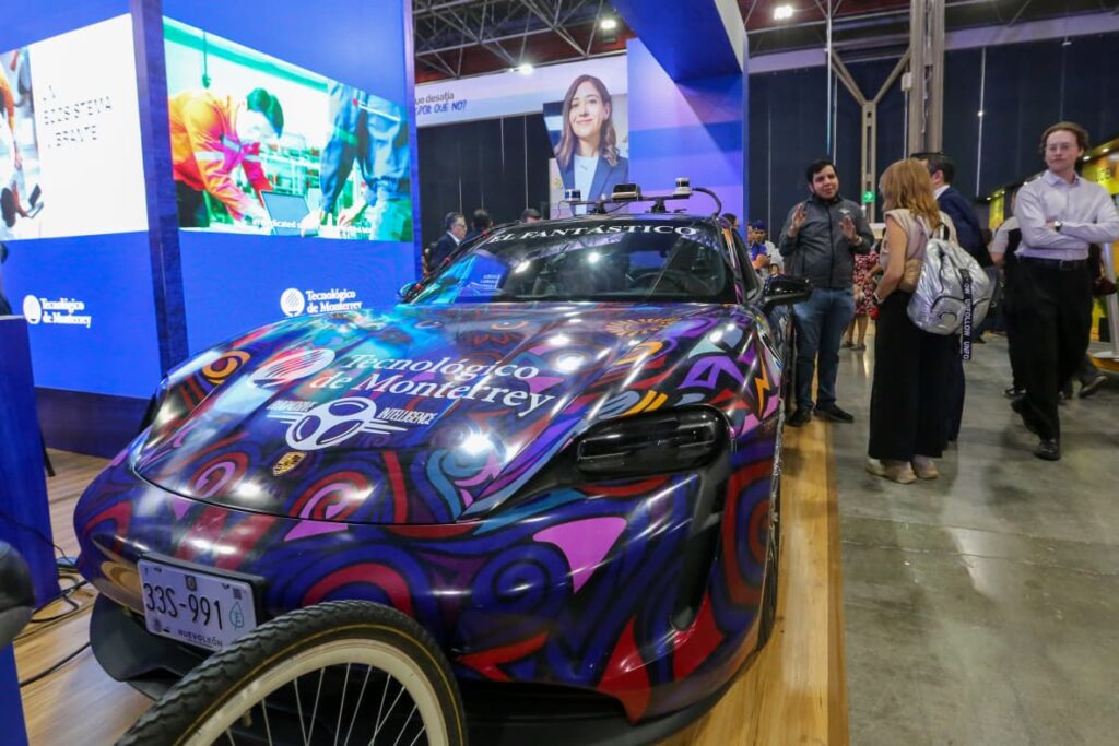 Colorful custom racing car on display at a technology expo, with people examining it in a convention hall.