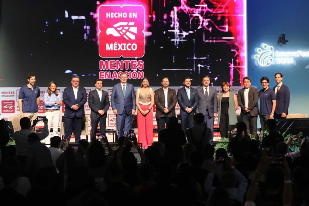 Group of diverse presenters and speakers on a stage at an event, with a large screen reading 'Hecho en México' and 'Mentes en Acción' in the background