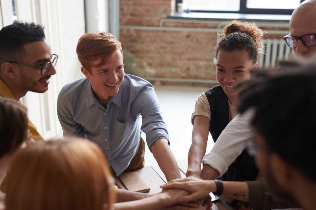 Diverse group of coworkers joining hands in the center of a table for a collaborative show of teamwork.