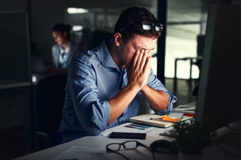 Persona agotada frente a una computadora refleja señales de desgaste y afectaciones a la salud mental en el trabajo.